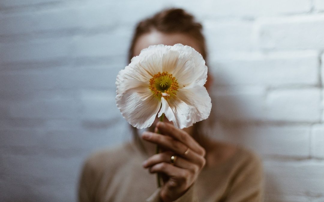 Mulher segurando uma flor e escondendo seus bloqueios emocionais
